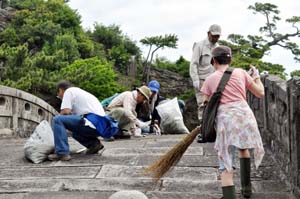不老橋の周辺や石のすき間の草を引く参加者たち - 和歌の浦で12団体合同の清掃活動