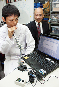 呼気マウスでパソコン操作する大学院生と北山准教授