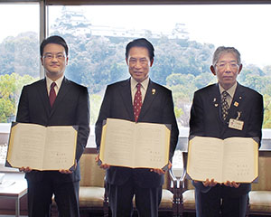 協定書を手に（左から）糟谷社長、尾花市長、藤本部長