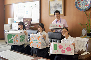 笑顔で段ボール箱を手にする（前列左から）岩本さん、谷口さん、黒川さんと濱田主任