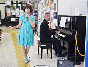 駅に設置されたピアノを弾く木谷さん㊨と歌い上げる宮本さん