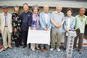 笑顔で石碑とパネルを囲む垣本さん（右から４人目）ら６期生の役員メンバー