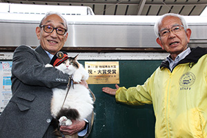 受賞記念プレートの前で木村代表㊨と小嶋社長㊧、ニタマ駅長